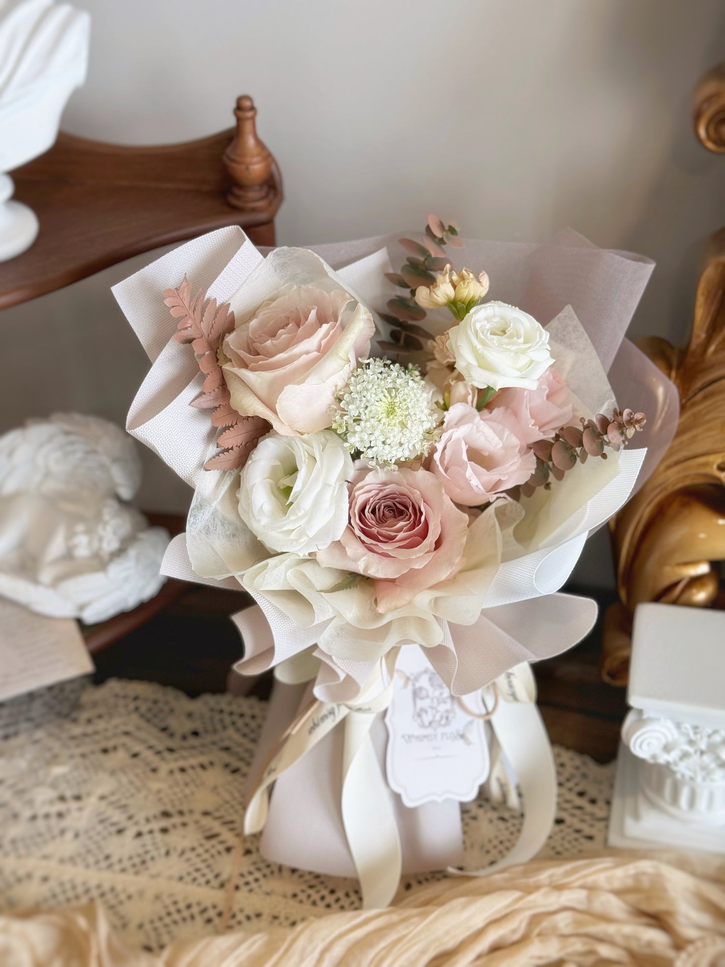 Pastel pink mixed fresh flowers bouquet in small (adorable) size. Dreamy pastel-toned bouquet placed on a table, showcasing its neutral elegance with quicksand roses and painted foliage.
柔棕粉色花束平放在木桌上，展现自然中性色调与玫瑰的优雅搭配。