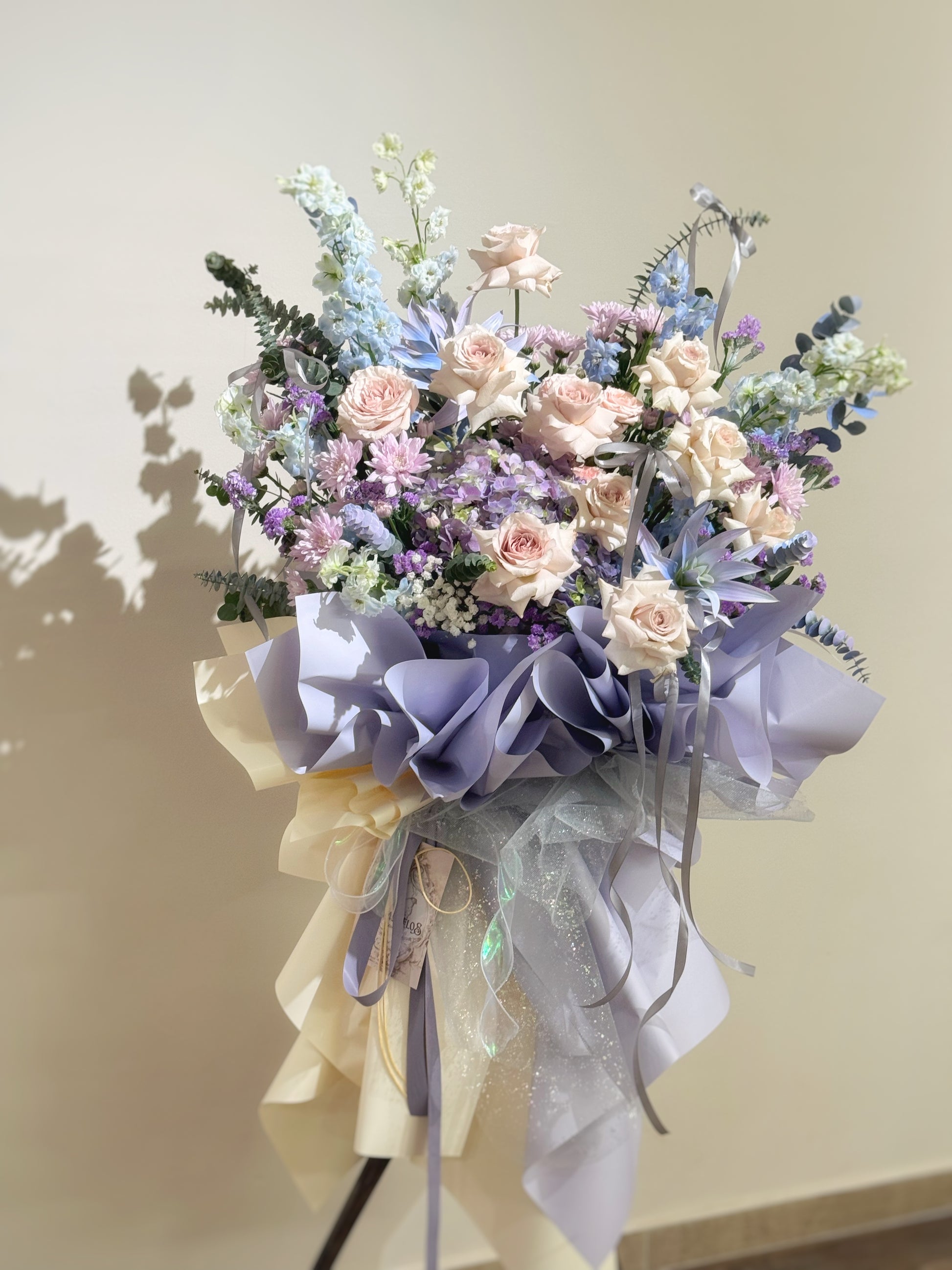 Close-up of fresh lilac, blush, and blue florals with spray-painted finishes, paired with lush greens and delicate filler flowers.
特写镜头聚焦柔紫、浅粉、蓝调鲜花与喷色质感，辅以绿叶与精致配花，细节丰富。