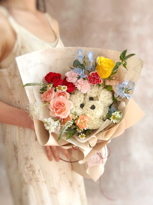 Bouquet of flowers shaped like a pup held by a person in a light dress. Front view of a playful bouquet with a puppy face crafted from white carnations, nestled among colorful fresh blooms and greens.

正面展示趣味花束，白色康乃馨打造的可爱小狗造型，周围点缀缤纷鲜花与绿叶，充满童趣与温馨感。