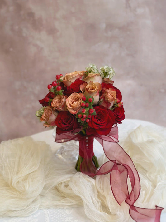 Round shaped fresh flowers bridal bouquet in nude pink and maroon color theme, featuring cappuccino roses, red Kenyan roses and other fillers. A perfectly symmetrical round bouquet featuring cappuccino roses and soft-toned florals, designed for a traditional Chinese wedding.
一款完美对称的圆形捧花，融合卡布奇诺玫瑰与柔和色调花卉，专为中式婚礼设计。