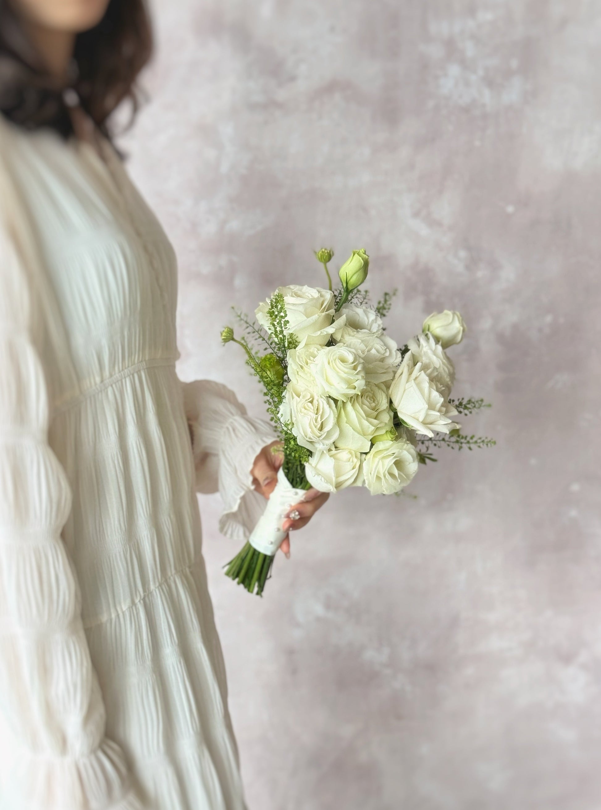 A model in white dress holding a timeless white bridal bouquet, elegantly designed with roses and eustoma flowers, held by a bride for a graceful wedding look
纯白玫瑰与洋桔梗打造轻盈浪漫的捧花，适合极简风格的新娘
