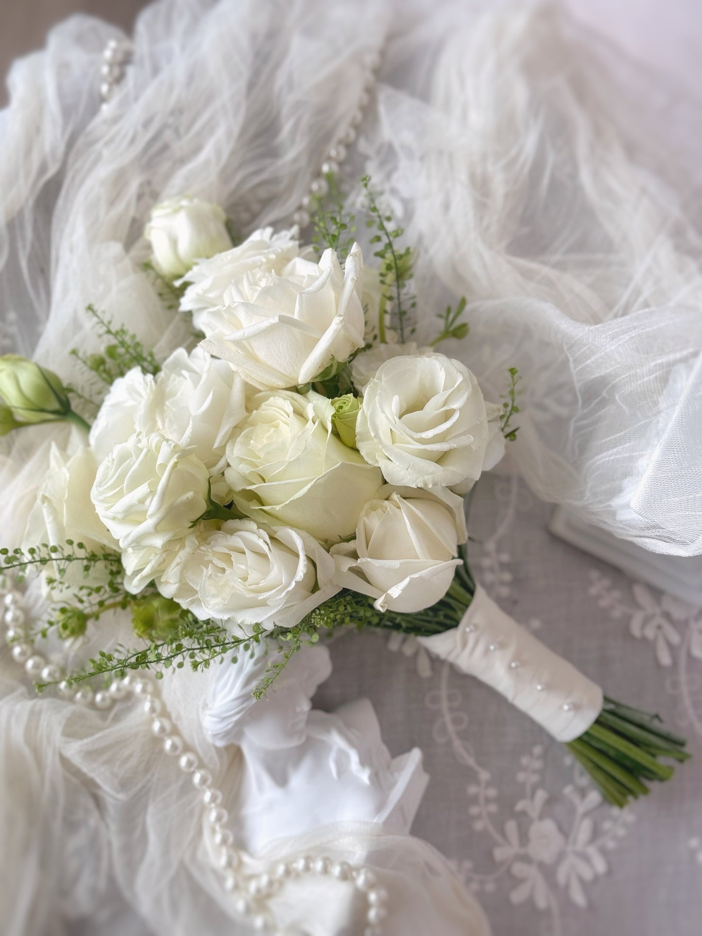 Top view of Chiffon bridal bouquet lying on a table with lace, Intricate floral details of a simple yet romantic white bridal bouquet, exuding sophistication and charm.
适合喜爱极简却不失精致感的新娘，纯白花艺设计
