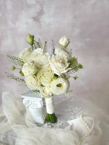Minimalist white bridal bouquet resting on a table, showcasing the delicate beauty of fresh roses and eustoma flowers.
简约优雅的韩式婚礼捧花，采用白色玫瑰与洋桔梗，散发纯净浪漫气息
