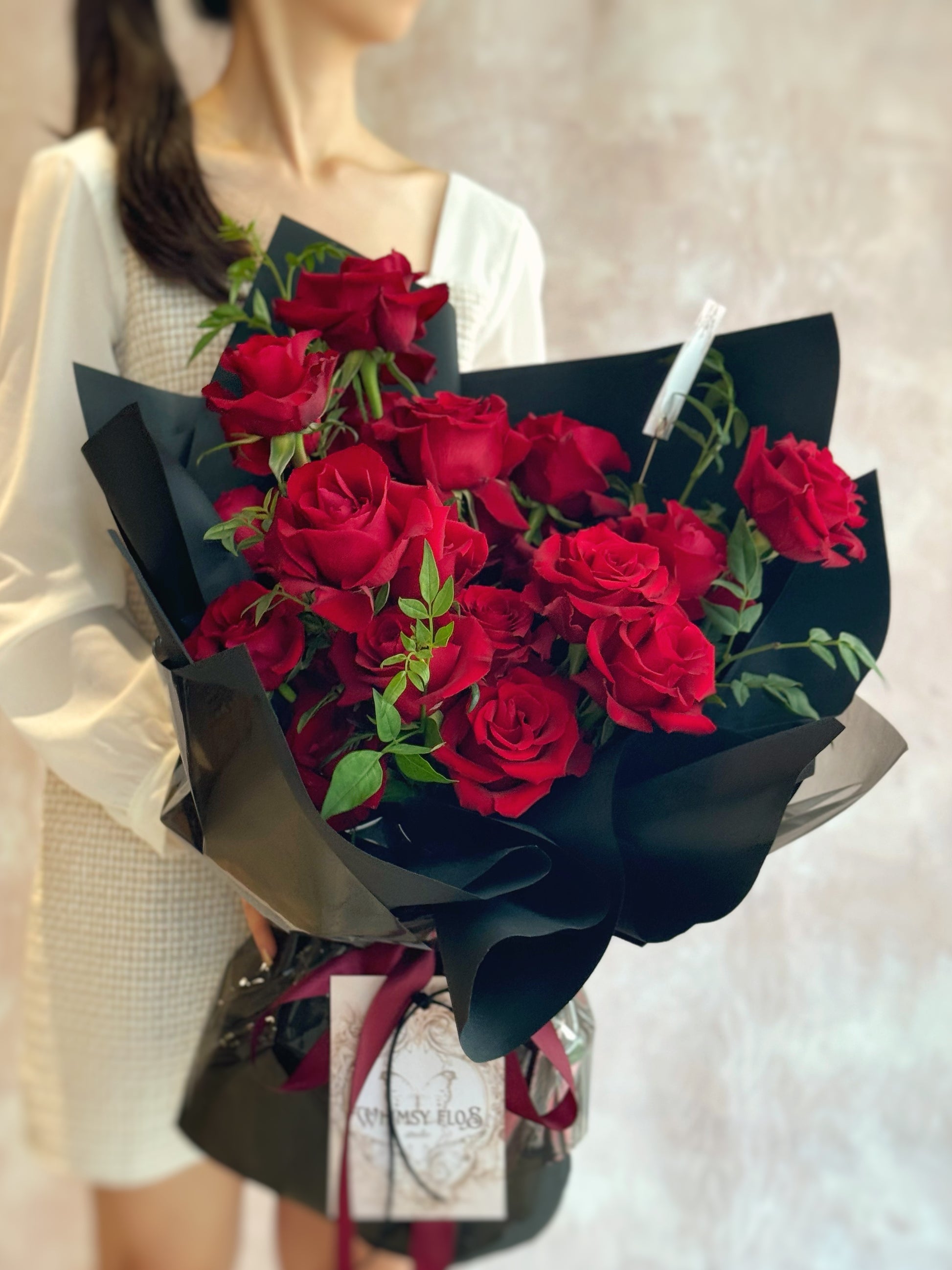 Model holding the Crimson Kiss bouquet—bold red roses wrapped in sleek black layers with a dramatic flair, perfect for passionate gestures. 模特手持Crimson Kiss花束，鲜红玫瑰搭配深黑色包装，展现强烈爱意与优雅气场。