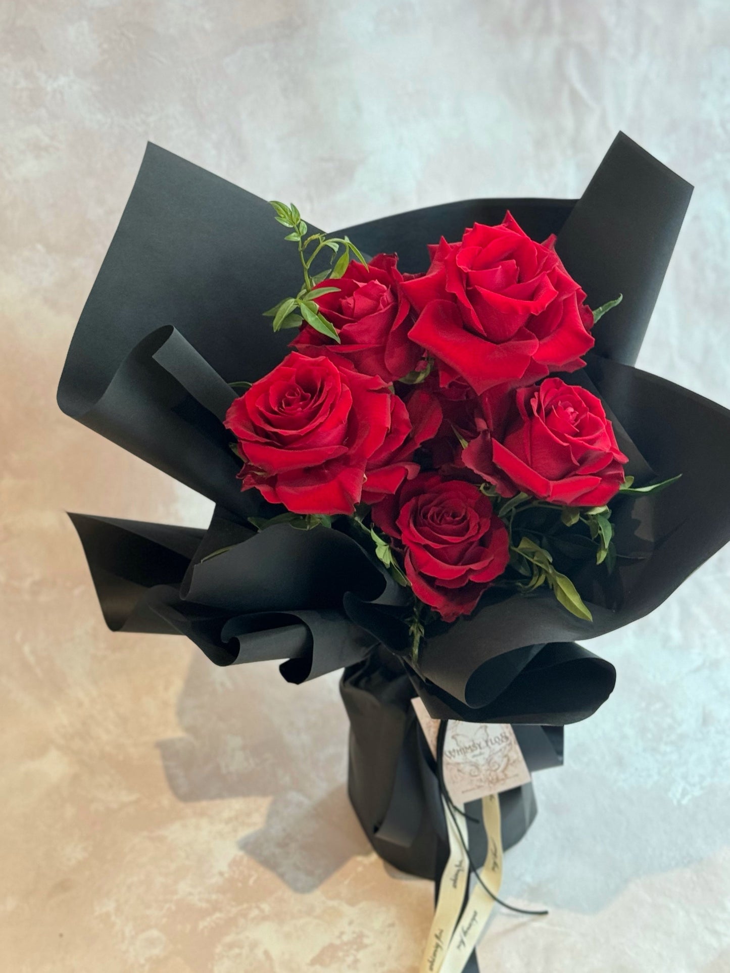 Close-up of Crimson Kiss bouquet, highlighting the lush red rose petals and sophisticated black wrapping layers.
Crimson Kiss花束近景图，细节展现饱满红玫瑰花瓣与光滑黑色包装纸的优雅结合。