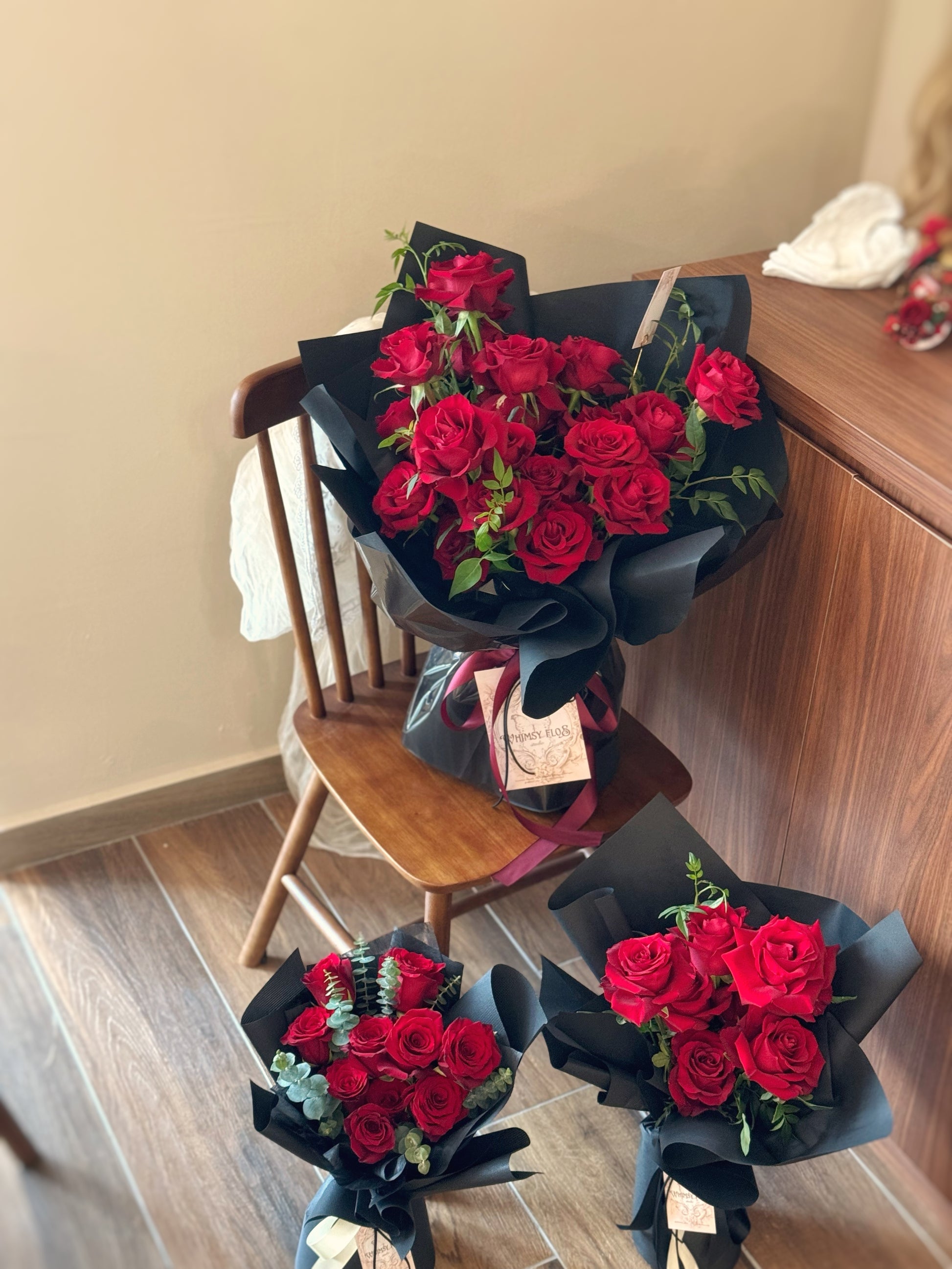 Crimson Kiss bouquet resting on a table, deep red roses contrasting elegantly with black wrapping for a powerful, refined look. Crimson Kiss花束静置在桌面上，红黑对比强烈，展现浓烈情感与高级质感。