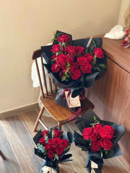 Crimson Kiss bouquet resting on a table, deep red roses contrasting elegantly with black wrapping for a powerful, refined look. Crimson Kiss花束静置在桌面上，红黑对比强烈，展现浓烈情感与高级质感。