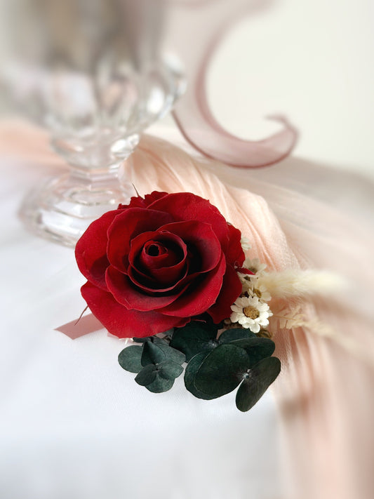 Close up view of a red preserved rose corsage accented with eucalyptus leaf and assorted fillers