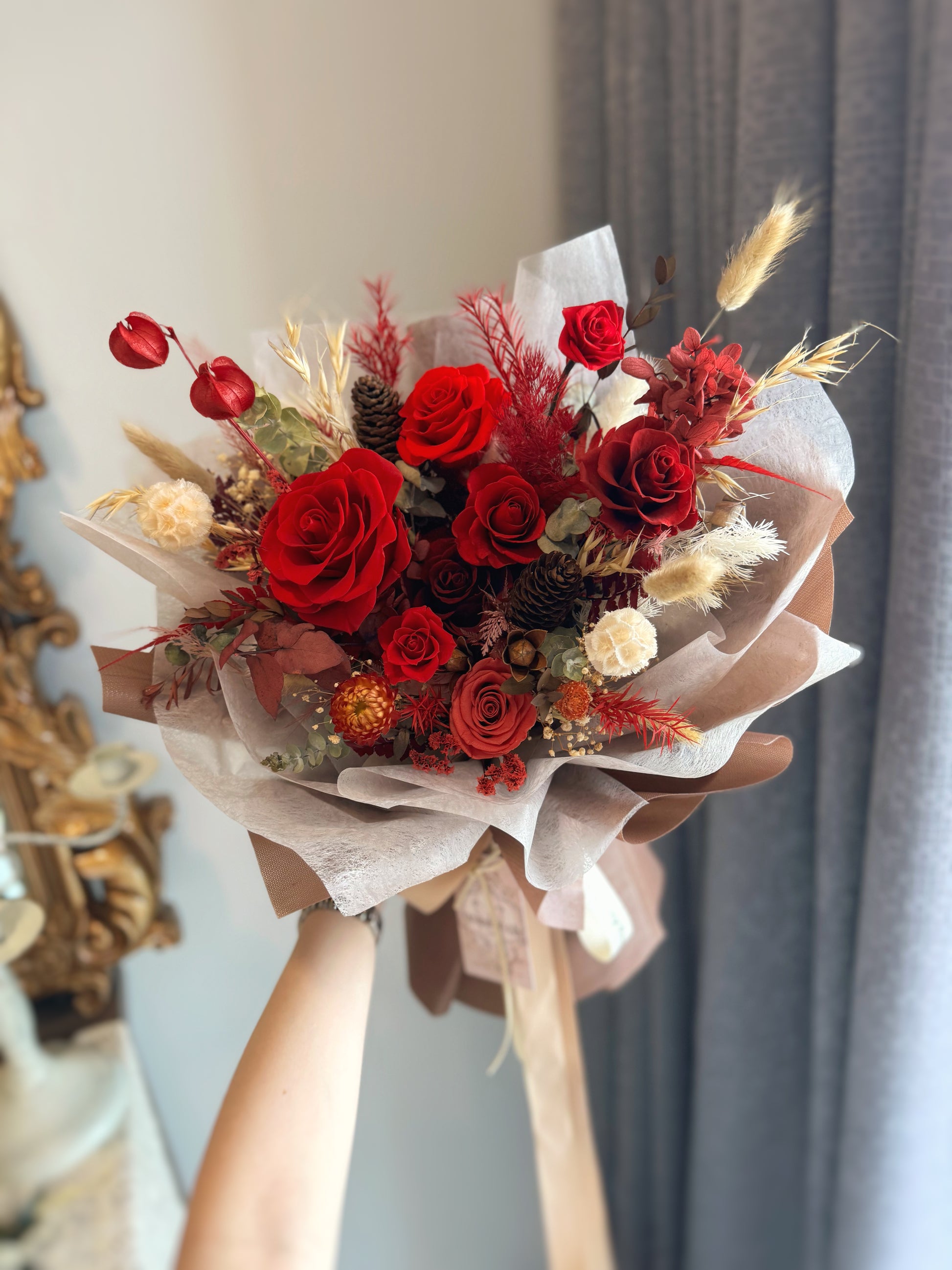 The Crimson Dusk bouquet held by hand, showcasing deep red and maroon preserved roses wrapped in earthy brown, exuding rustic elegance and timeless sophistication.
“Crimson Dusk” 花束手持展示，深红和酒红色的永生玫瑰包裹在大地棕色花束中，散发着乡村优雅与永恒的高贵感。