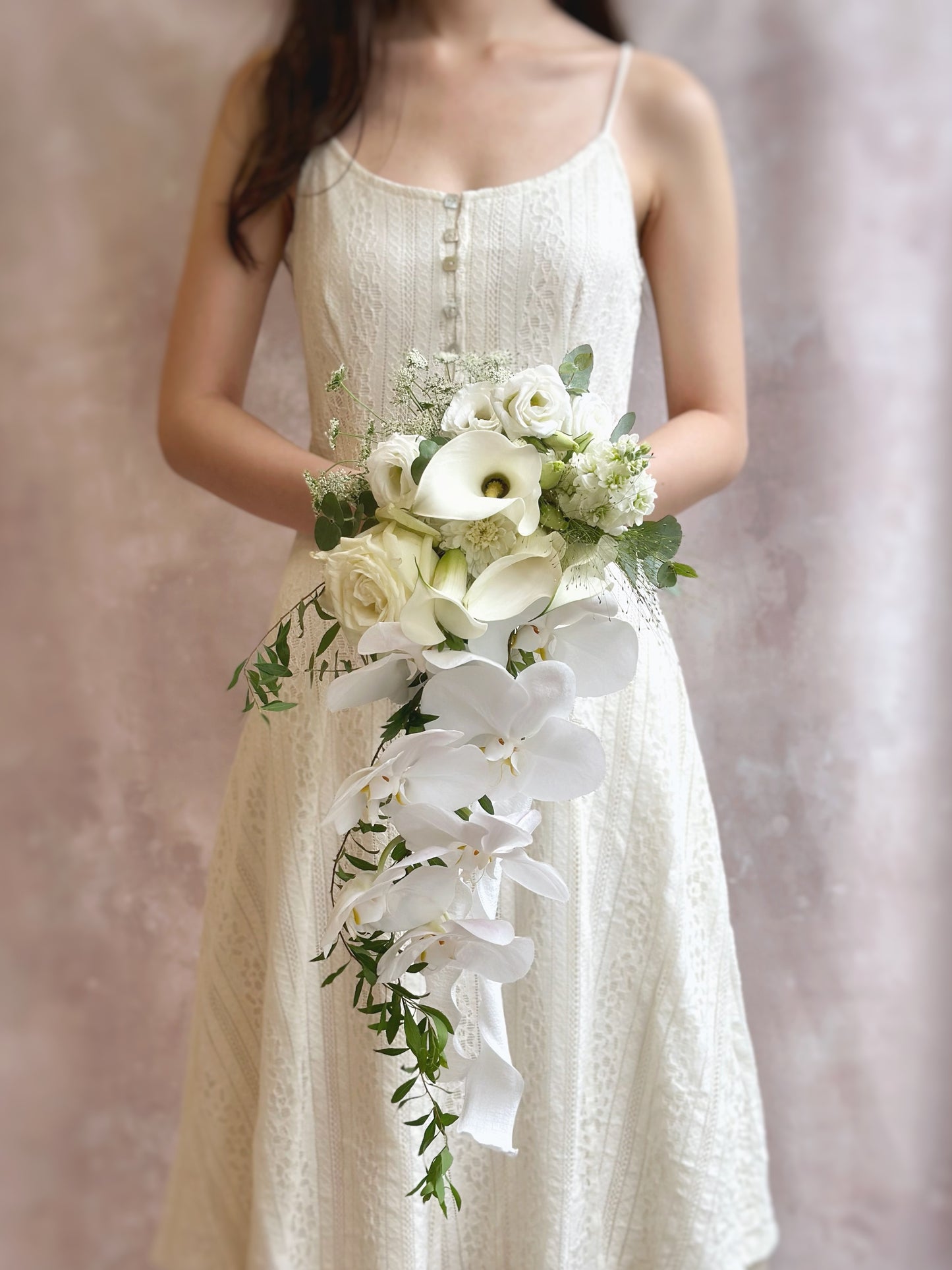 Delicate orchids and calla lilies arranged in a modern teardrop bouquet
现代泪滴形捧花，搭配精致的蝴蝶兰与马蹄莲