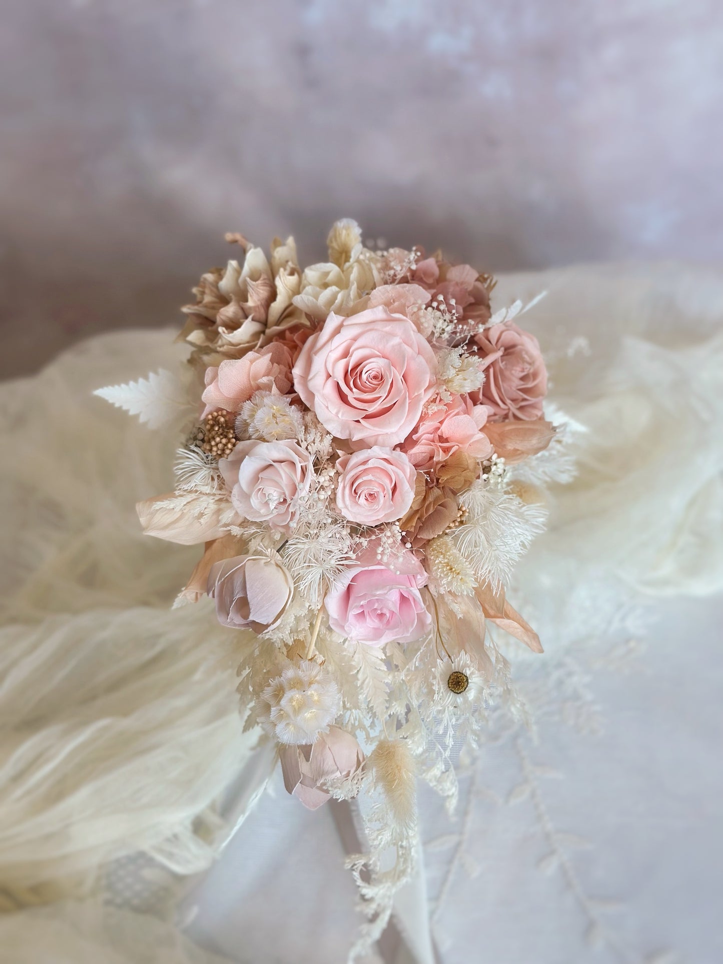A cascading preserved bridal bouquet with a soft peachy pink to white ombré transition, exuding grace and elegance.
一款渐变色的瀑布形永生花新娘捧花，从柔和蜜桃粉到纯净白色，散发优雅气质。