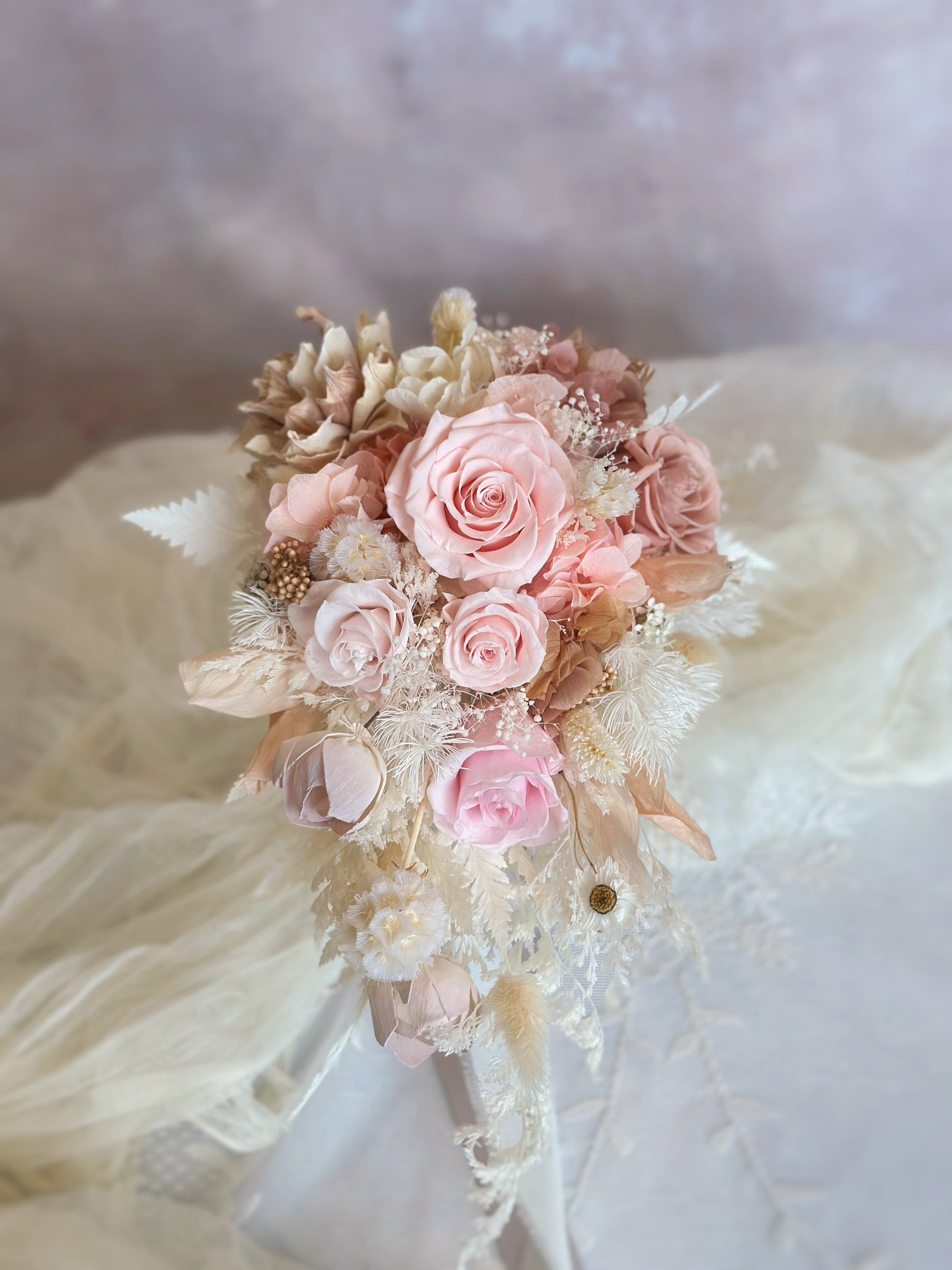 A cascading preserved bridal bouquet with a soft peachy pink to white ombré transition, exuding grace and elegance.
一款渐变色的瀑布形永生花新娘捧花，从柔和蜜桃粉到纯净白色，散发优雅气质。