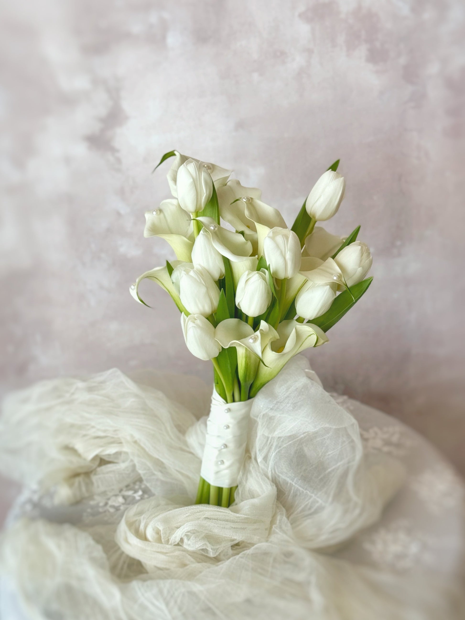 Front view of Genuine fresh flowers bridal bouquet, a minimalist bridal bouquet featuring elegant calla lilies and tulips, arranged on a table for a clean and modern look. 与传统新娘花束不同，这款郁金香与马蹄莲捧花展现极简优雅风格

