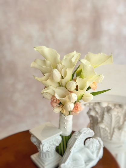 Front view of a minimalist bridal bouquet featuring sleek white calla lilies, soft tulips, and warm nude peach spray carnations.

正面展示简约新娘花束，结合优雅白色马蹄莲、柔和郁金香及暖色调裸粉色小康乃馨。