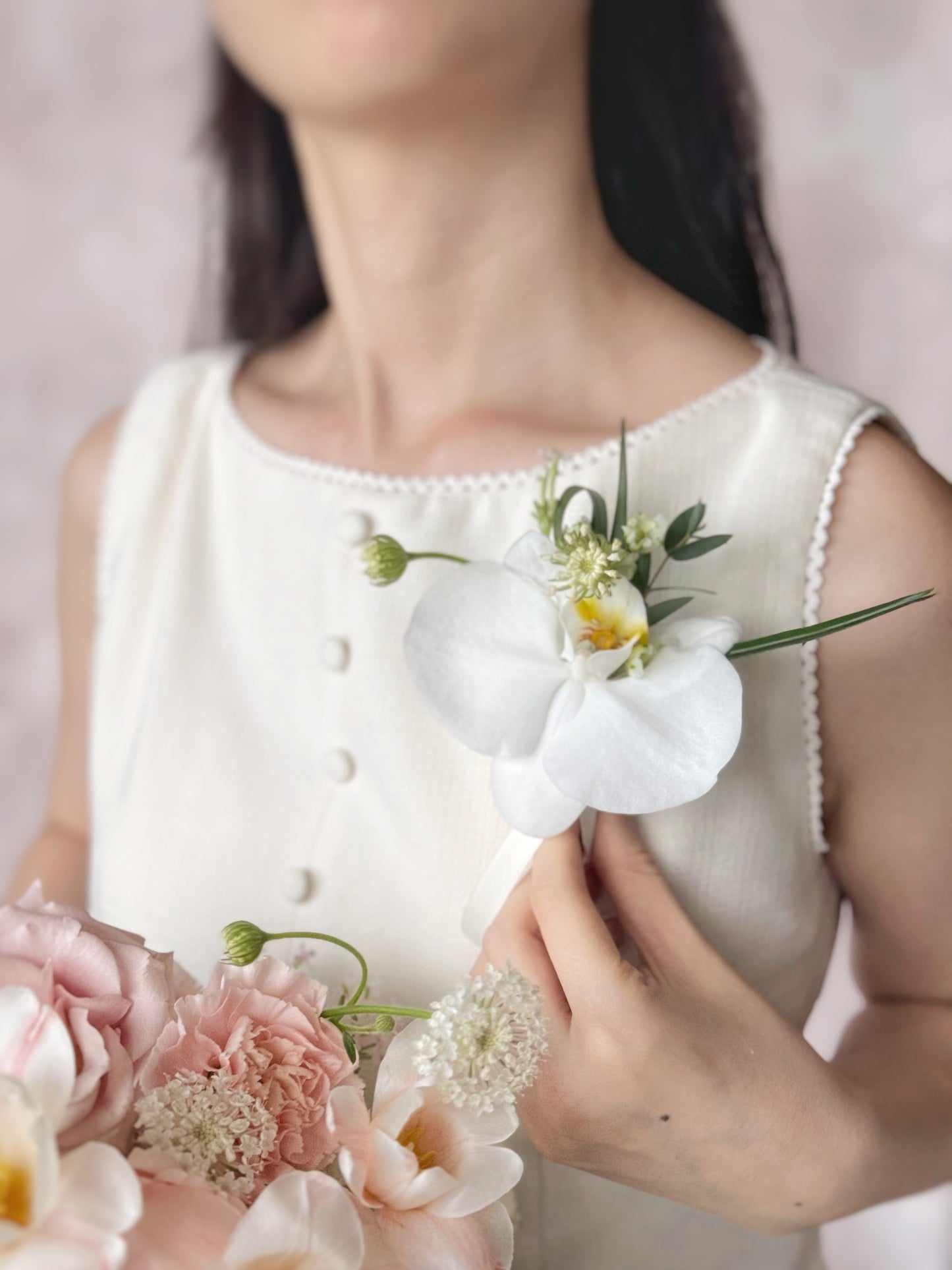 Model wearing an elegant Phalaenopsis orchid corsage with seasonal fillers and foliage, showcasing its graceful and timeless design