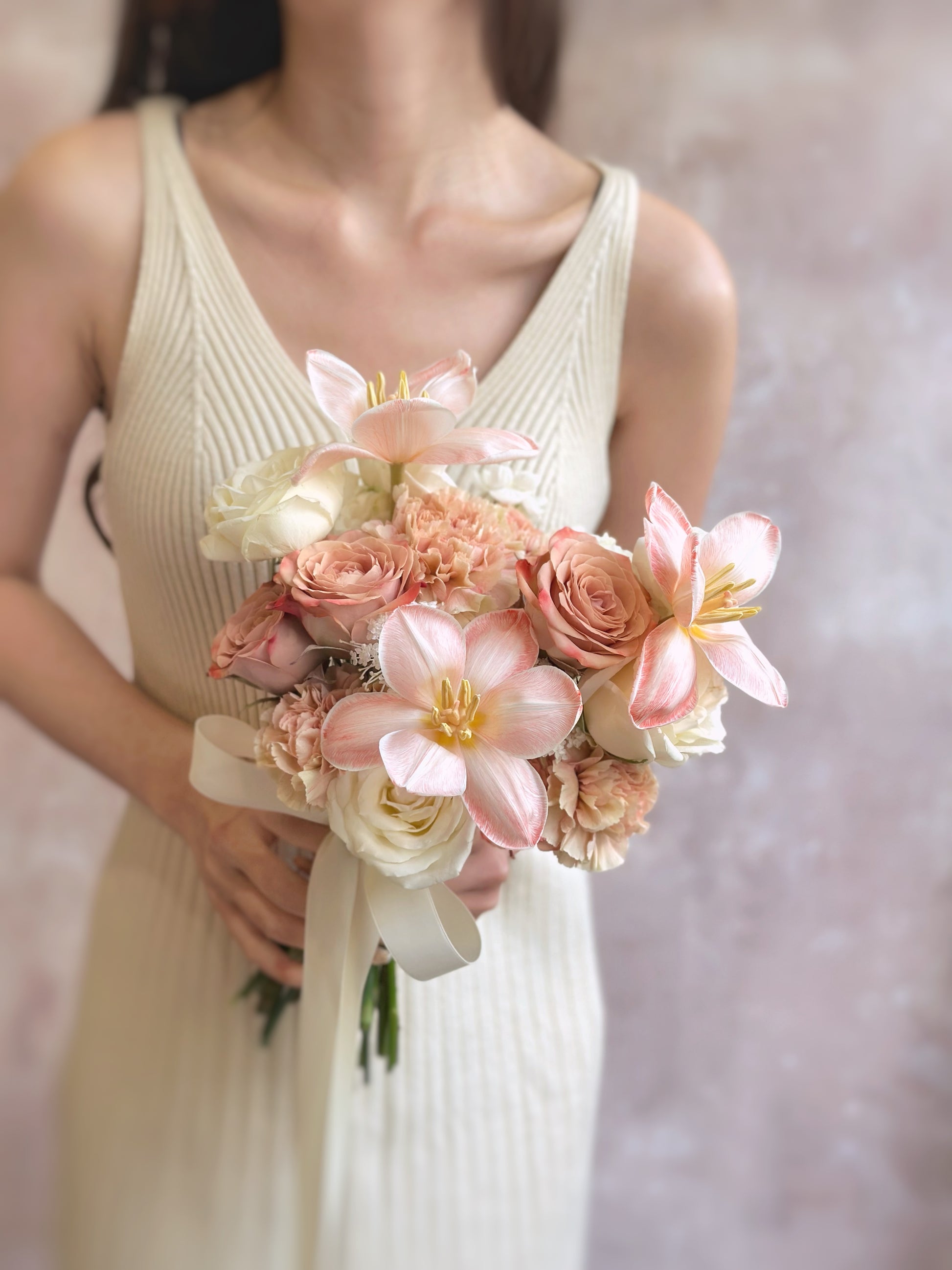A bride gently holding a heart-shaped bouquet of peachy apricot pink tulips and pastel cream florals, radiating femininity and romance.
新娘手持心形捧花，由蜜桃杏粉色郁金香与奶油色花卉组成，散发出女性柔美与浪漫气息。