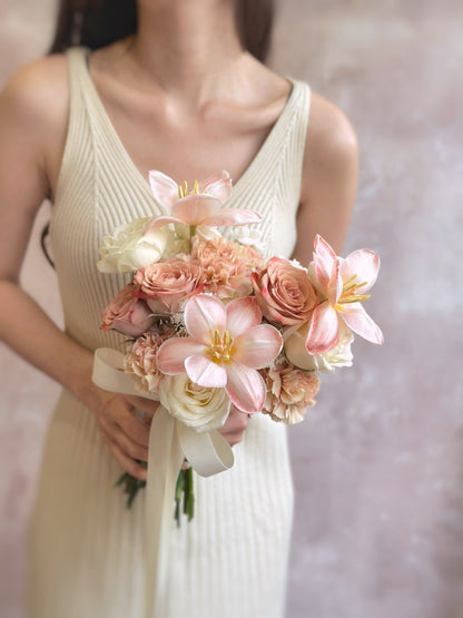 A bride gently holding a heart-shaped bouquet of peachy apricot pink tulips and pastel cream florals, radiating femininity and romance.
新娘手持心形捧花，由蜜桃杏粉色郁金香与奶油色花卉组成，散发出女性柔美与浪漫气息。