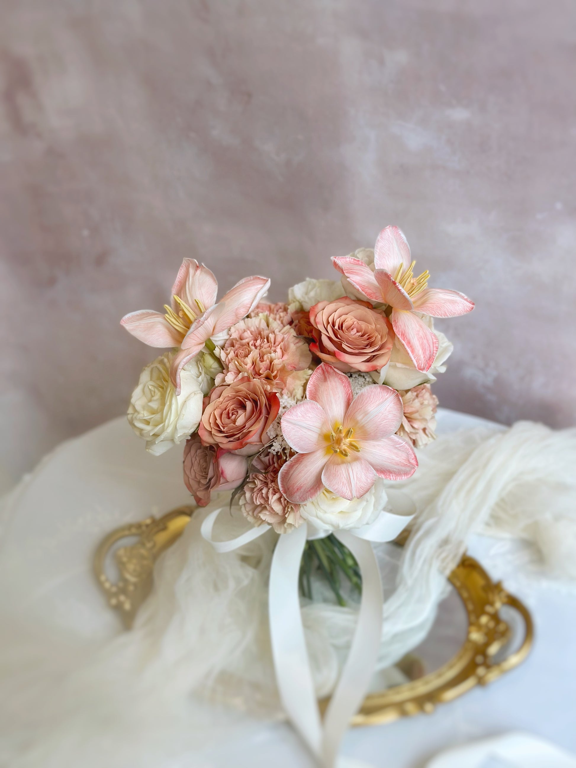 A delicate and romantic blush-toned bouquet resting on a soft fabric backdrop, highlighting the dreamy peachy apricot tulips as the centerpiece.
甜美裸粉色调捧花安放在柔软布料上，梦幻的蜜桃杏粉色郁金香成为亮点。


