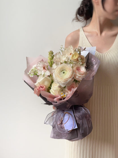 Side angle of the bouquet highlighting the layering of blush and cream blooms against lavender wrapping.
从侧面拍摄，展示花束中粉色与奶油色花朵的层次感，配以薰衣草灰包裹纸。