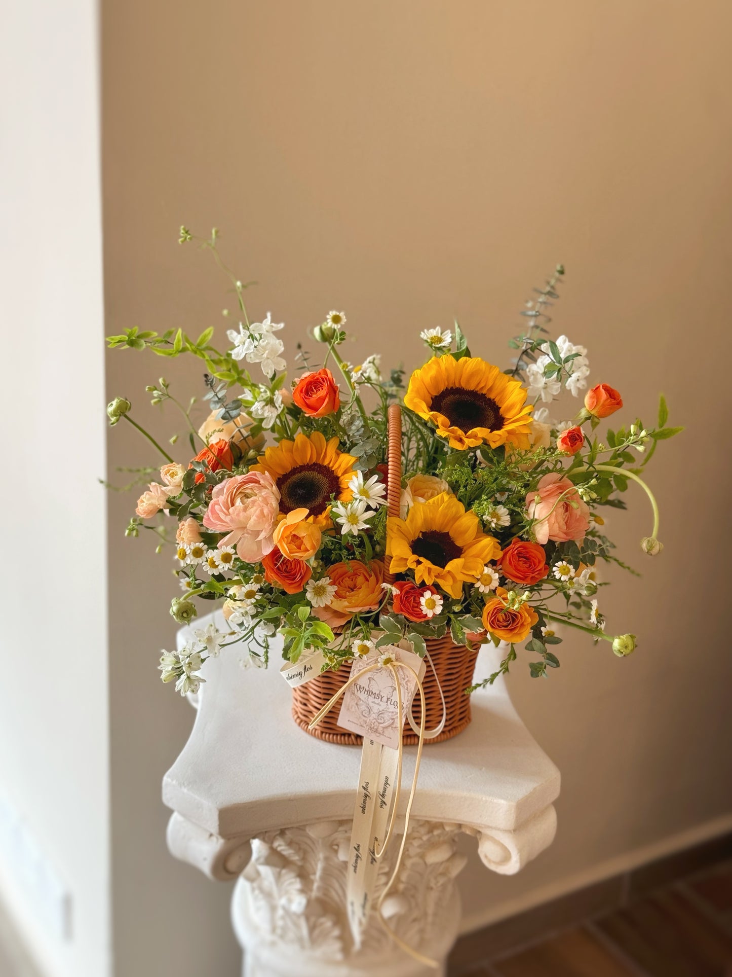 Front view of a vibrant basket arrangement with sunflowers, orange and yellow blooms, and abundant green foliage, radiating warmth and cheer.
正面展示充满阳光感的花篮，向日葵搭配橙黄花朵与繁茂绿叶，散发温暖与喜悦氛围。