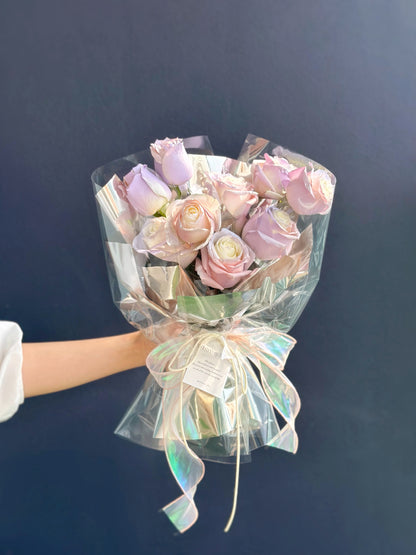 Delicate roses, spray-painted in shades of pastel pink, blue, and lilac, dance gracefully amidst a galaxy-themed wrapping paper