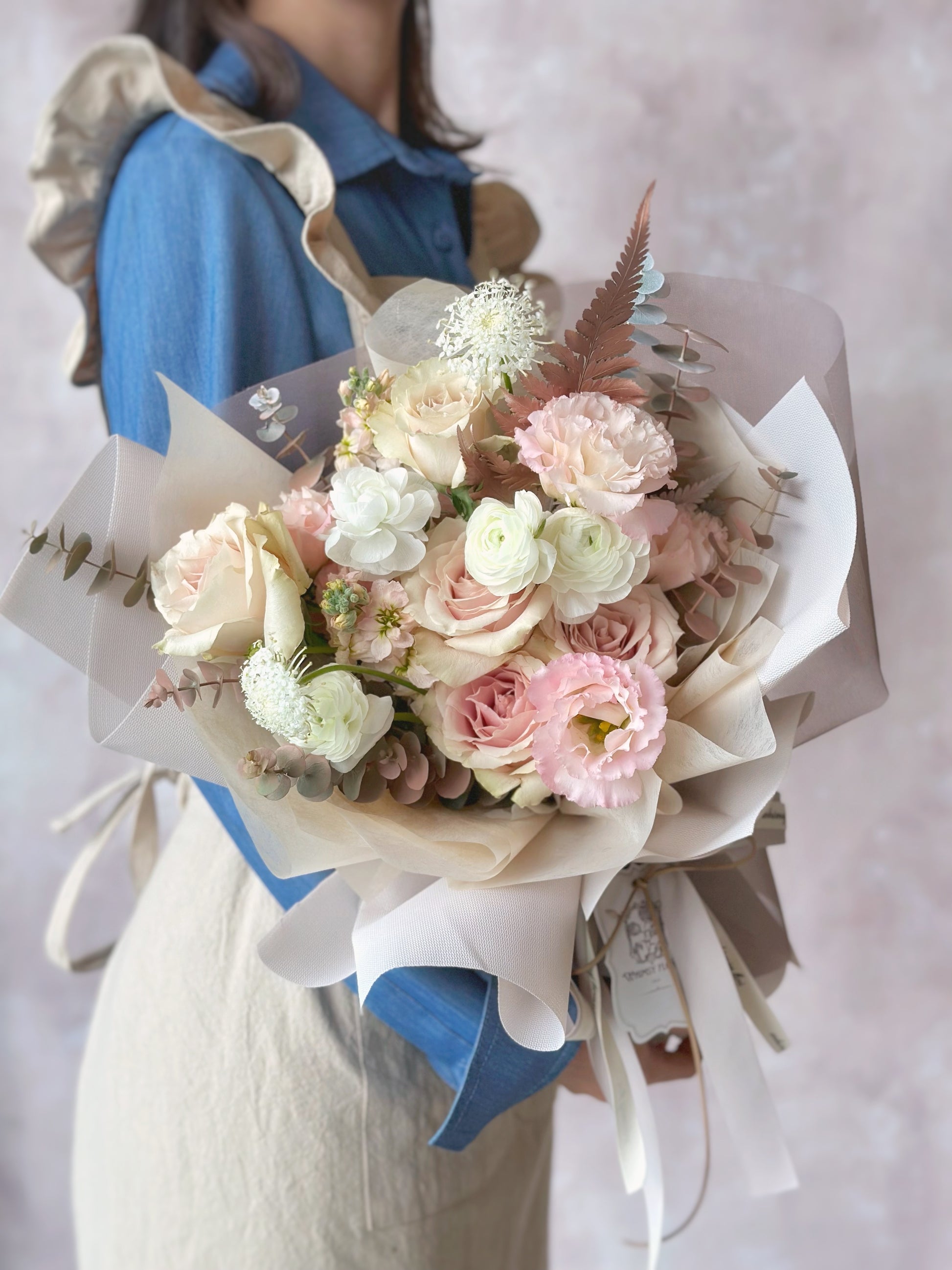 Holding a grand size pastel blush pink tone bouquet, consisting of roses, eustoma, ranunculus, lace flowers, spray painted foliage and other fillers 