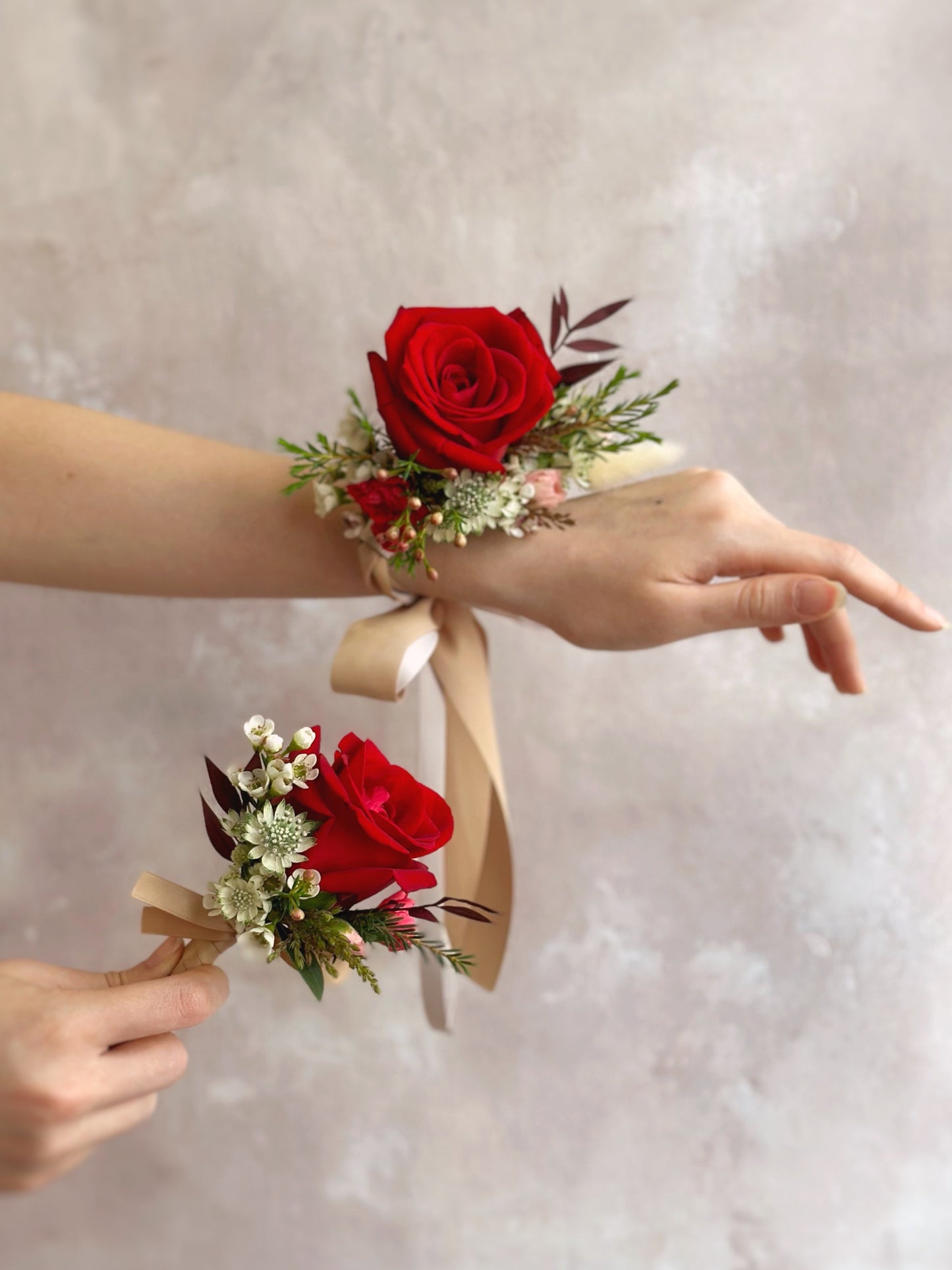 A set of red roses wrist corsage and boutonnière with lush greeneries 