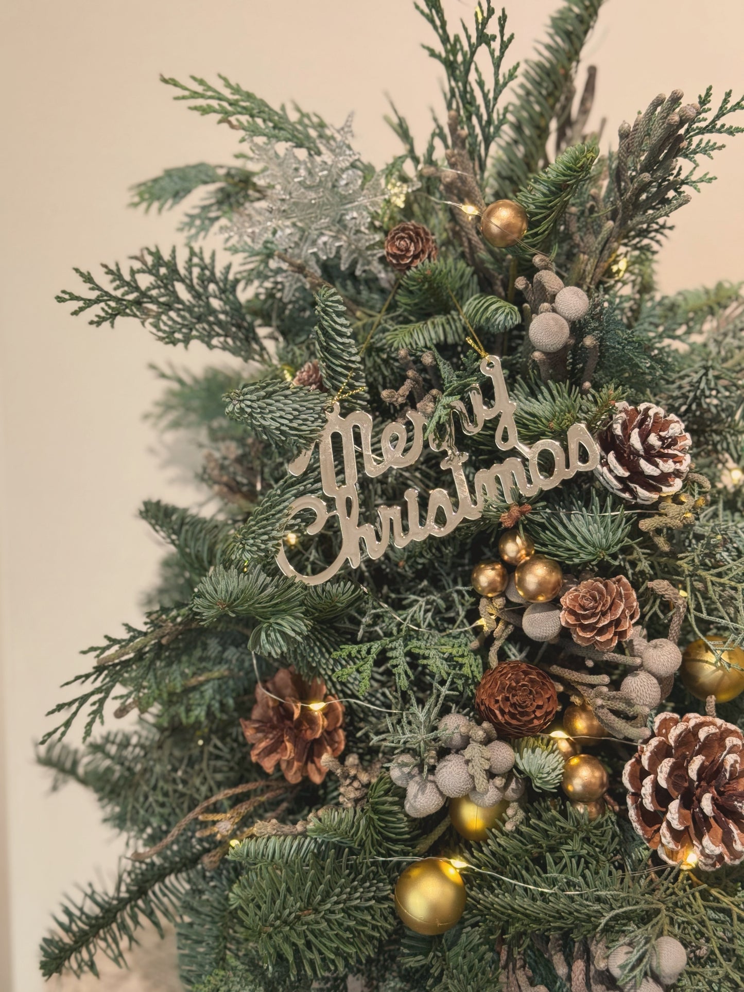 Close-up of assorted fir branches, pinecones, silvery flowers, and gold accents on the “Into the Wood” Christmas tree.
 “Into the Wood” 圣诞树细节特写，展示混合松枝、松果、银色花材和金色点缀。