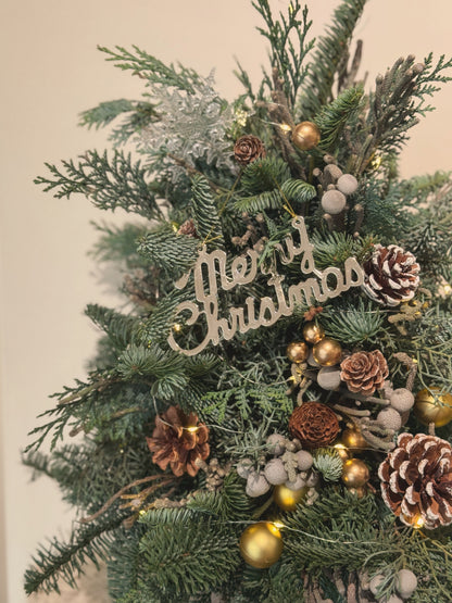 Close-up of assorted fir branches, pinecones, silvery flowers, and gold accents on the “Into the Wood” Christmas tree.
 “Into the Wood” 圣诞树细节特写，展示混合松枝、松果、银色花材和金色点缀。