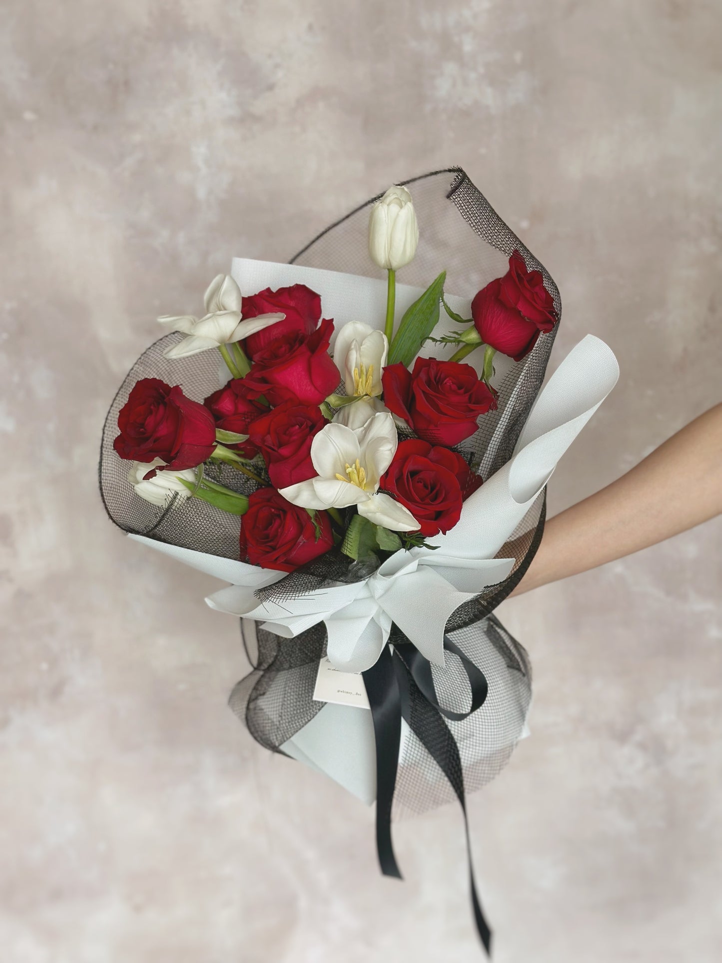 A bouquet of red roses and white tulips wrapped with black lace and white paper and tied with a black ribbon.