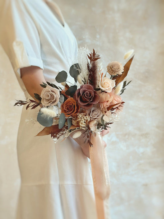 A bride holding the Katniss bouquet, its earthy tones beautifully complementing an autumn wedding.
新娘手持Katniss捧花，大地色调完美契合秋季婚礼氛围。