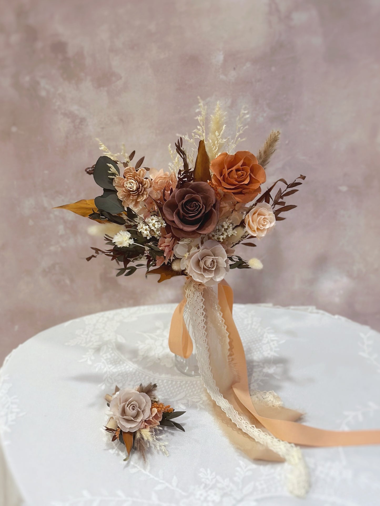 A matching corsage featuring a burnt orange preserved bloom with soft pampas grass and greenery.
搭配胸花，采用焦橙色永生花、柔和芦苇草与绿叶点缀。