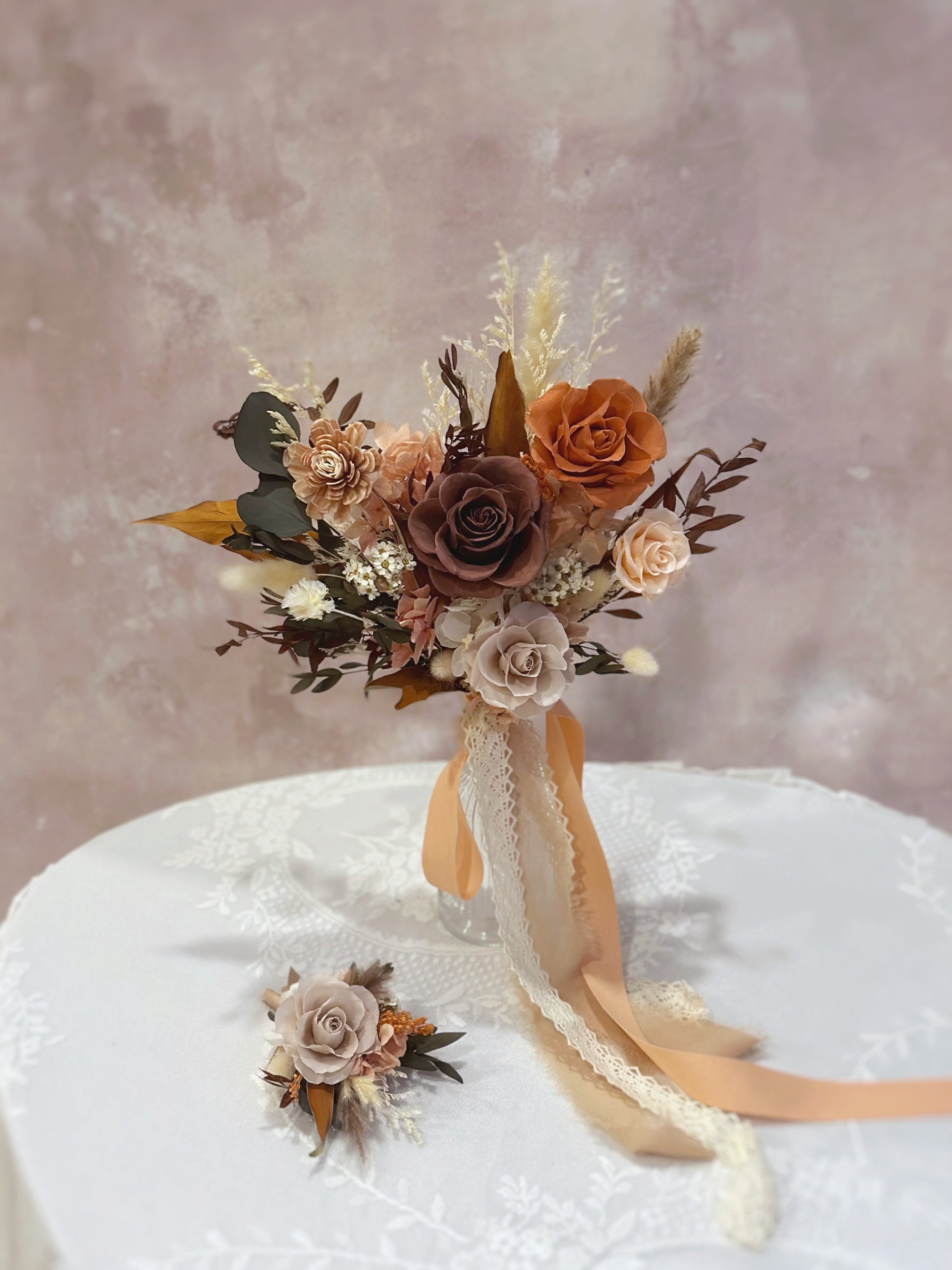 A matching corsage featuring a burnt orange preserved bloom with soft pampas grass and greenery.
搭配胸花，采用焦橙色永生花、柔和芦苇草与绿叶点缀。