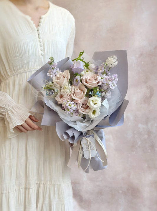 Lilac princess fresh flowers handtied bouquet in luxe size, held by model on front view. Front view of a whimsical lilac and baby blue bouquet with soft cool-toned flowers. 正面展示带有梦幻淡紫与婴儿蓝色调的冷感系花束全貌。