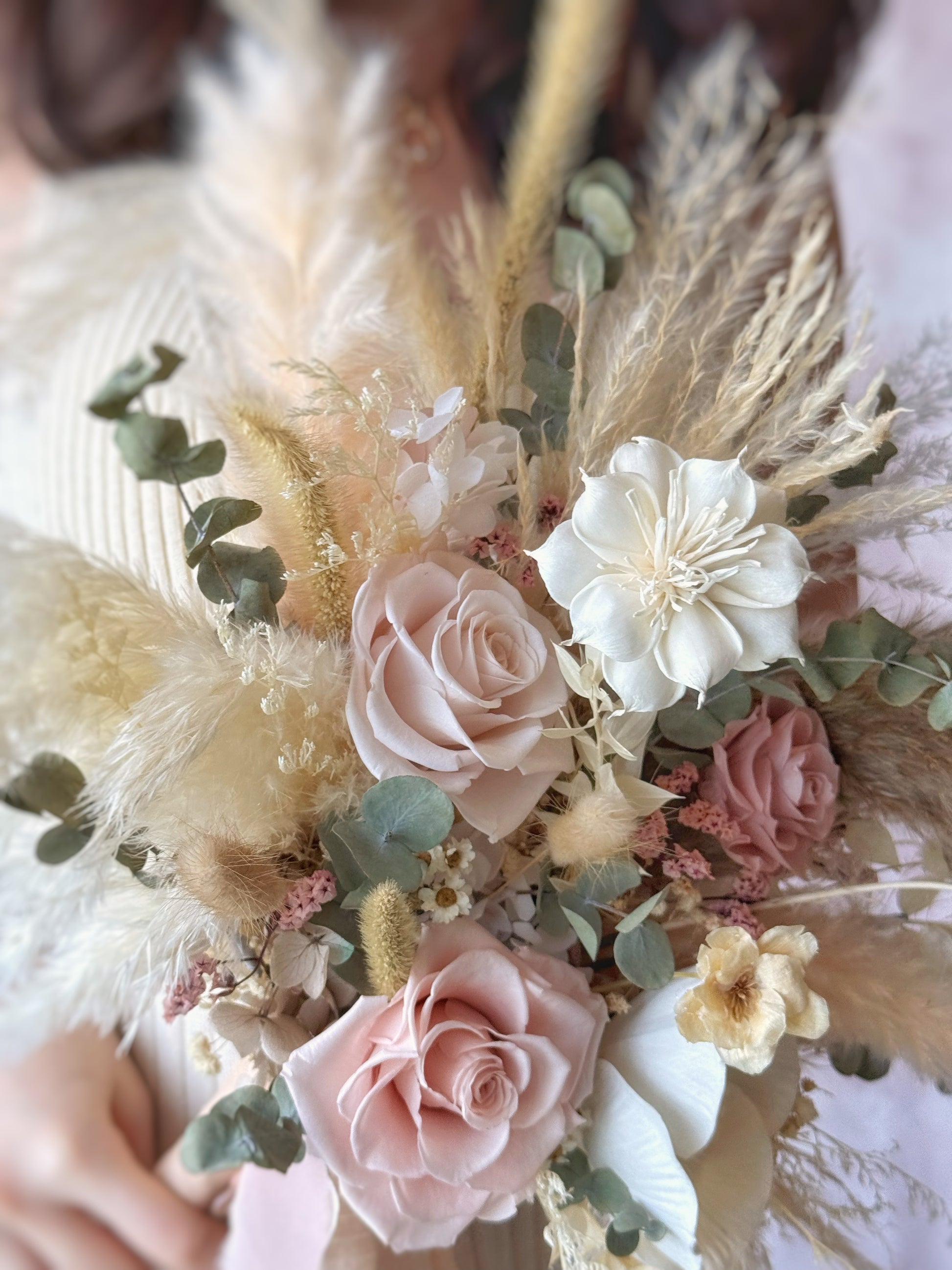 Linnea preserved flowers fan shaped bridal bouquet bohemian style close up view. Delicate preserved blooms and wispy pampas grass create an ethereal and organic look.
永生花搭配轻盈的芦苇草，营造出梦幻而自然的视觉效果。

