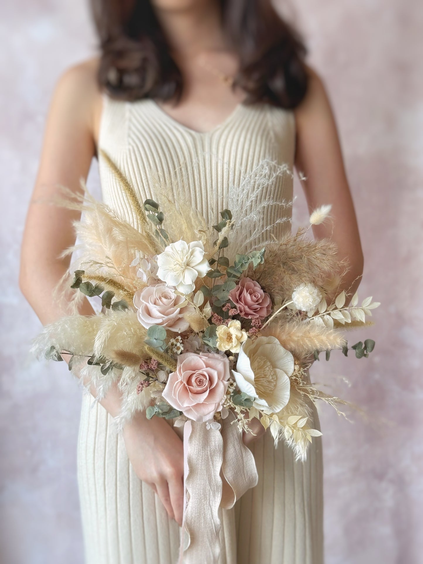 A bride holding the fan-shaped bouquet, its cascading dried elements adding a free-spirited and bohemian touch.
新娘手持扇形捧花，流畅的干花线条增添自由洒脱的波西米亚风格。