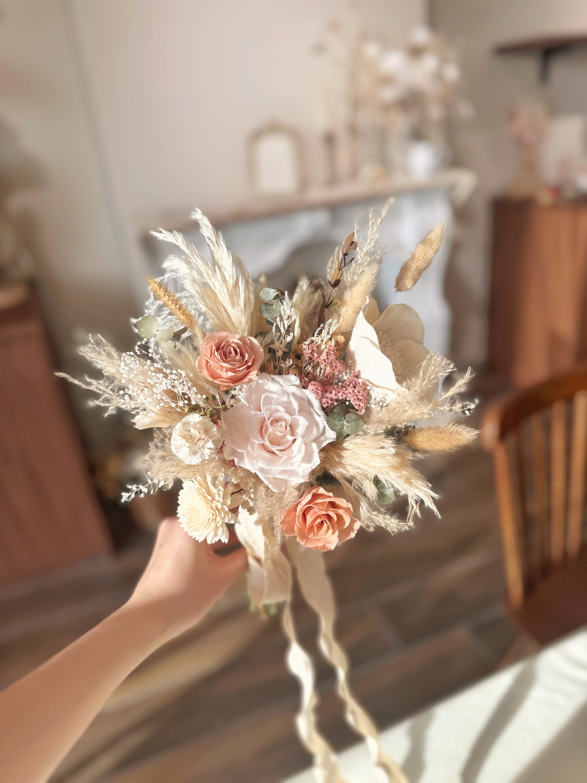 The soft, nude pink and cream tone bohemian-style bridal bouquet held in hand, showcasing its natural textures and warm hues.
