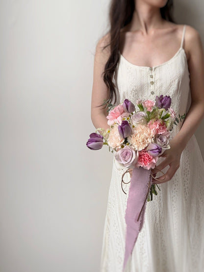 A dreamy bridal bouquet featuring purple tulips, pink roses, and pastel blooms, beautifully arranged for a soft and whimsical wedding look. Ideal for brides who love a candy-colored floral theme.