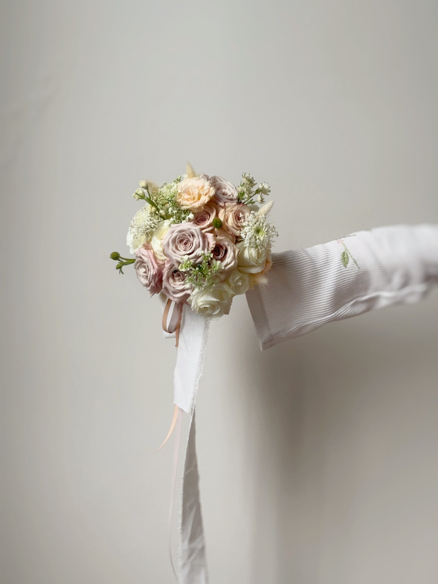 A model gently holding the pastel-hued round bouquet, with soft nude blush roses beautifully arranged for an elegant and romantic touch.
新娘手持裸粉色圆形捧花，柔和玫瑰精美排列，散发优雅浪漫气息。

