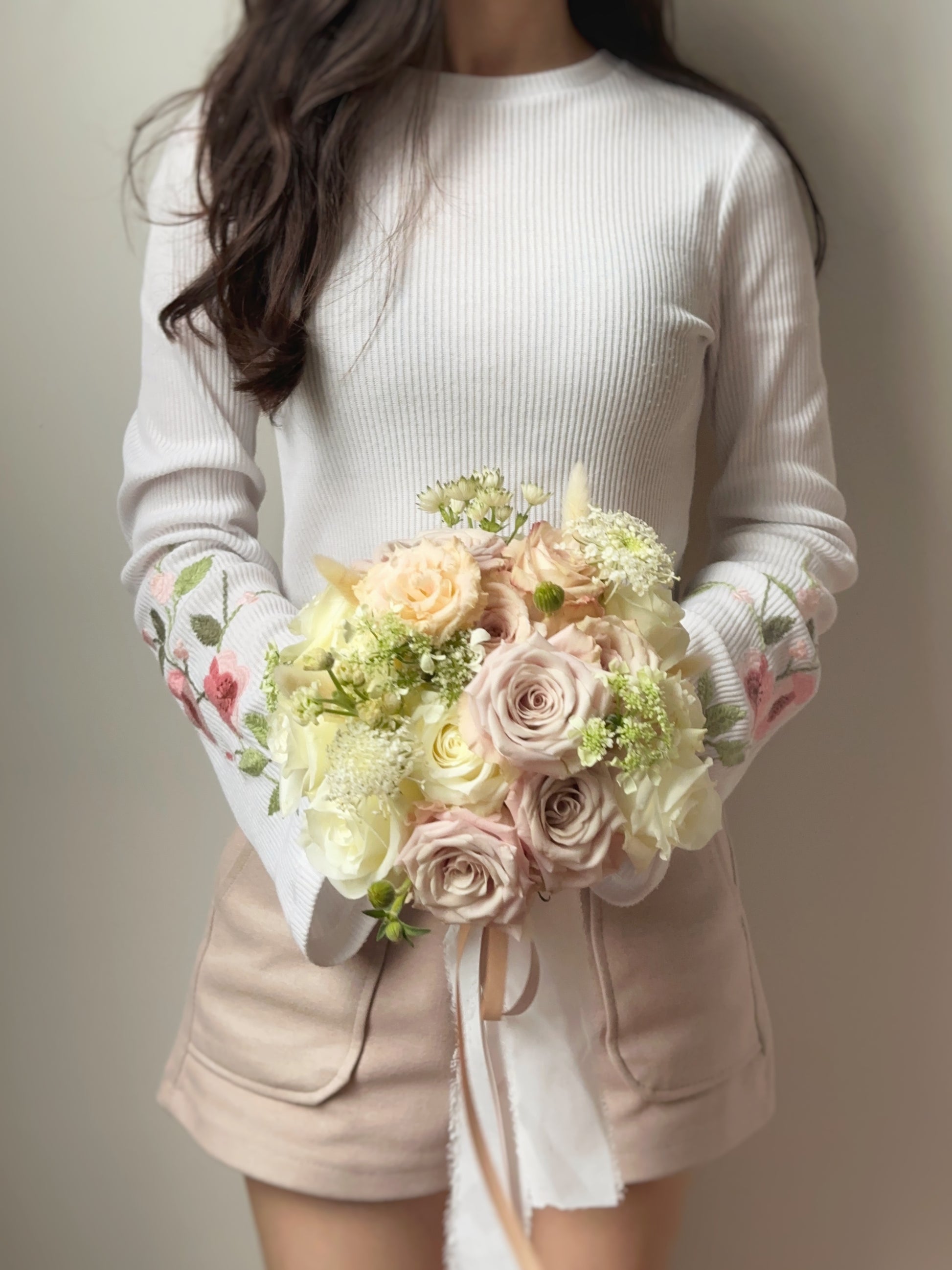 The round shaped fresh pastel rose bouquet being held in front of the model, complementing her bridal look with soft and timeless floral beauty.
新娘手持捧花，搭配婚纱，散发柔和而永恒的花卉之美。