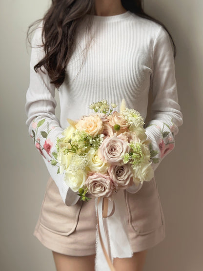 The round shaped fresh pastel rose bouquet being held in front of the model, complementing her bridal look with soft and timeless floral beauty.
新娘手持捧花，搭配婚纱，散发柔和而永恒的花卉之美。