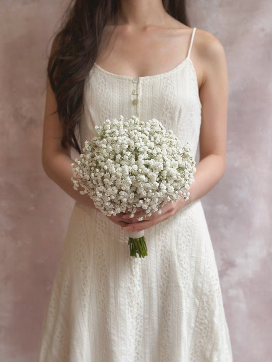 Bride holding a round bouquet of white baby’s breath in front of her, timeless and elegant
新娘手持圆形满天星捧花，经典优雅