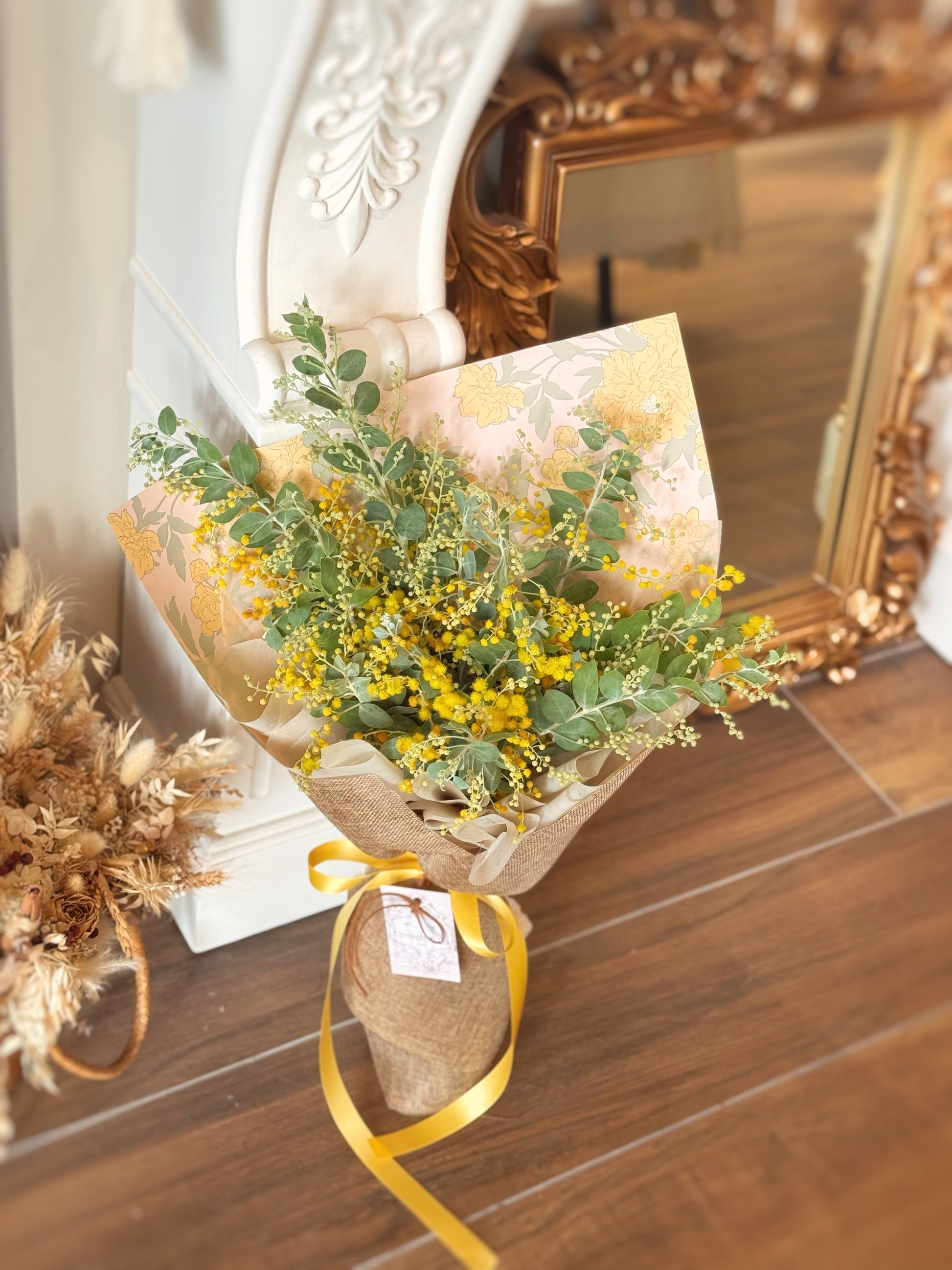 Bouquet of yellow mimosa acacia flowers wrapped in brown paper with a yellow ribbon on a wooden floor.