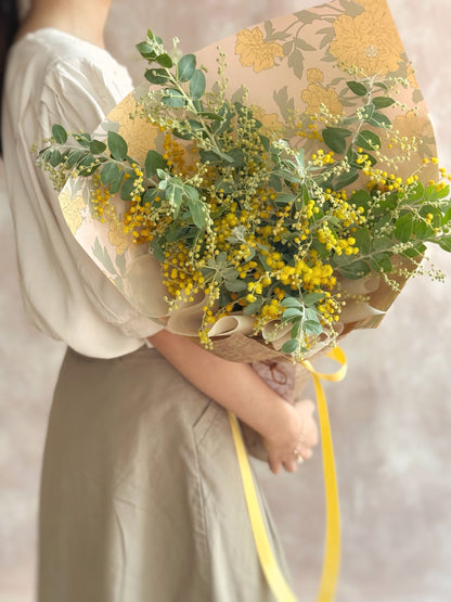 Model holding Golden Glow bouquet with sunny yellow acacia blooms, adding a cheerful touch to festive styling.
 模特手持 Golden Glow 花束，明亮黄色合金欢花，为节日布置增添阳光感。