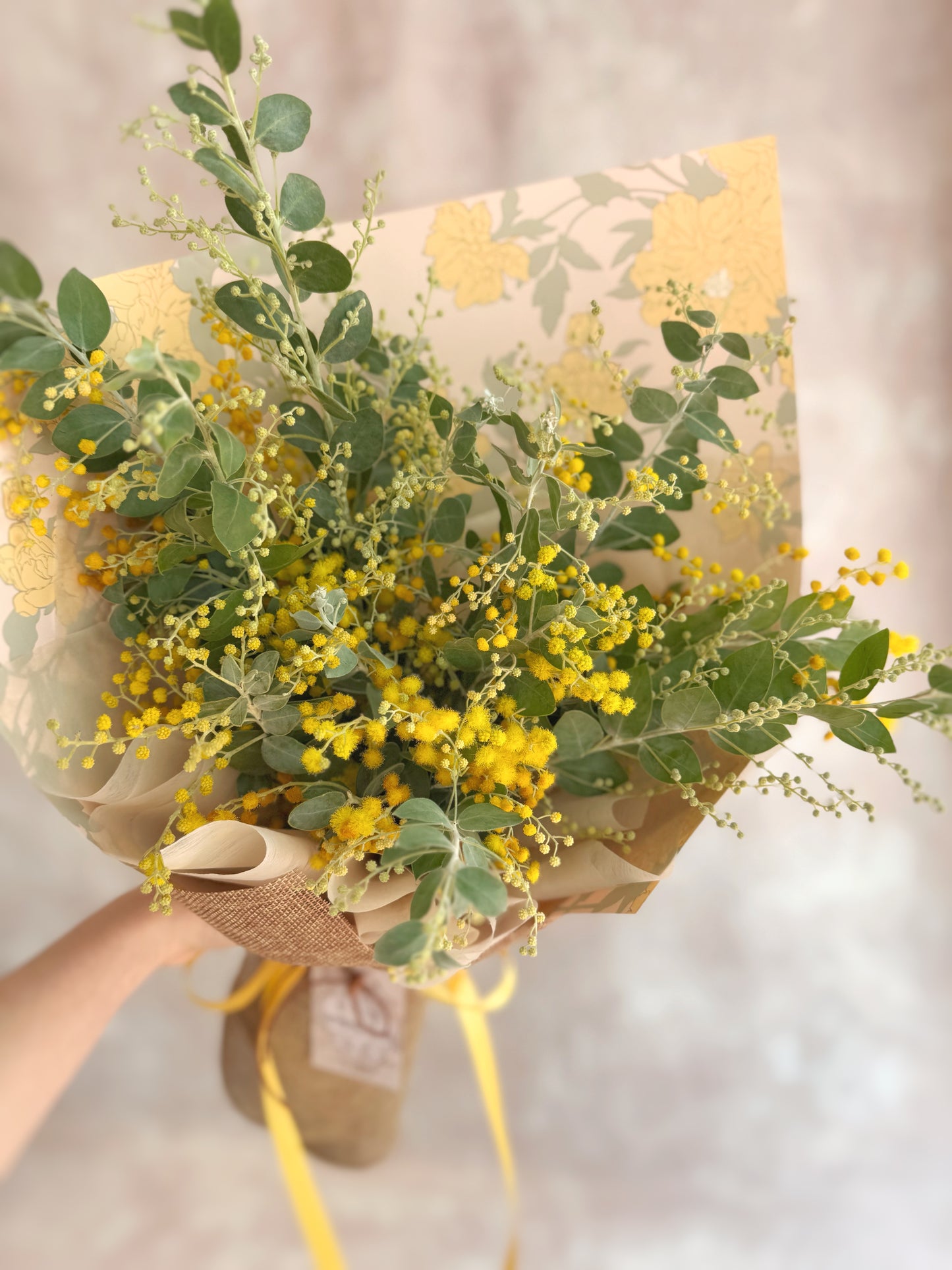 Model holding a delicate Golden Glow bouquet of fluffy yellow acacia blooms for a modern holiday look.
模特手持精致 Golden Glow 花束，绒球状黄色相思花，呈现现代节日风