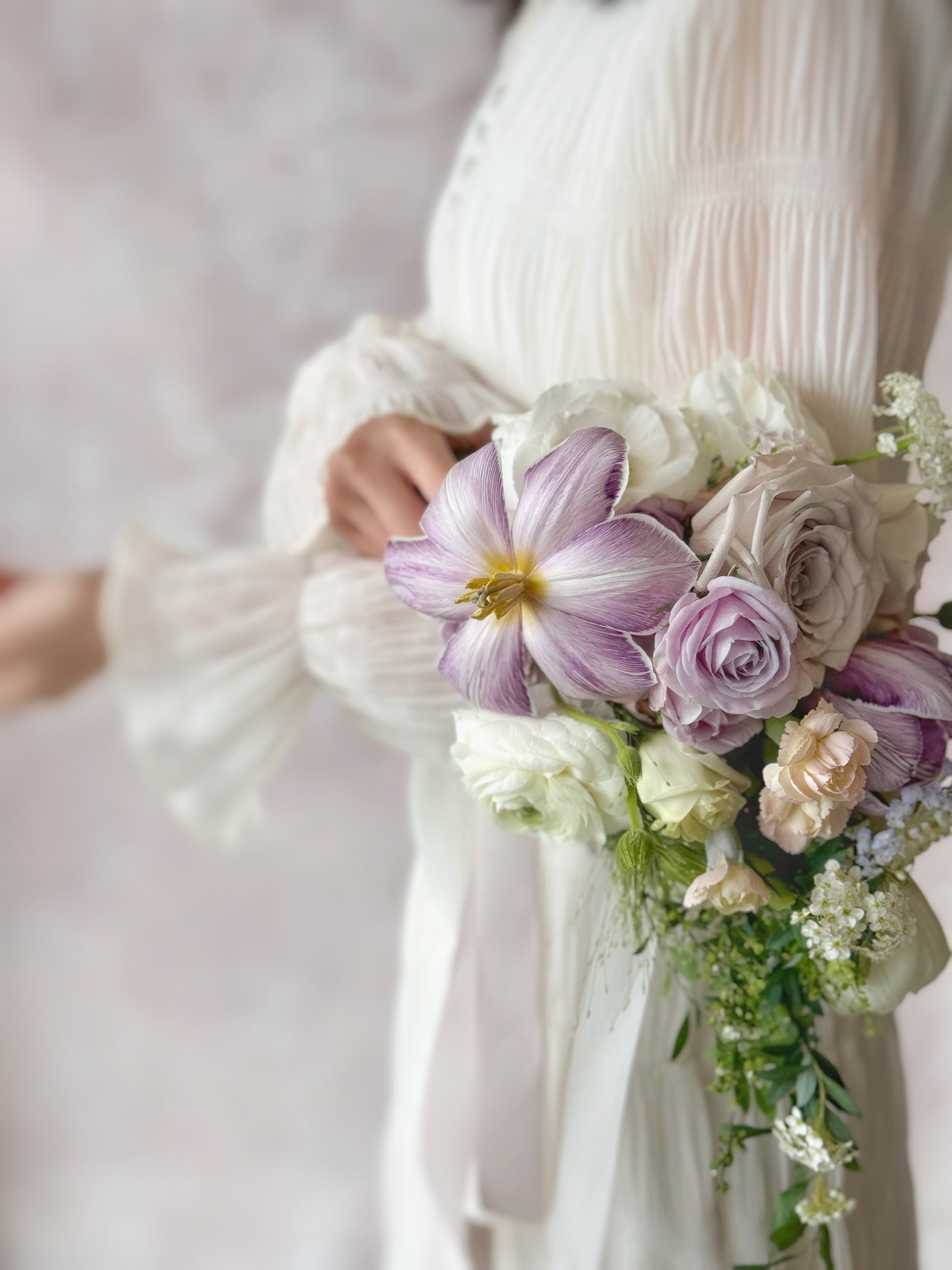 Side closed up view of Ocean eyes teardrop bridal bouquet held by a model, showing elegant floral details, with violet tulips, soft lilac and white orchids creating a natural, flowing silhouette