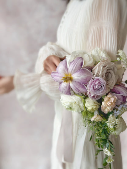 Side closed up view of Ocean eyes teardrop bridal bouquet held by a model, showing elegant floral details, with violet tulips, soft lilac and white orchids creating a natural, flowing silhouette