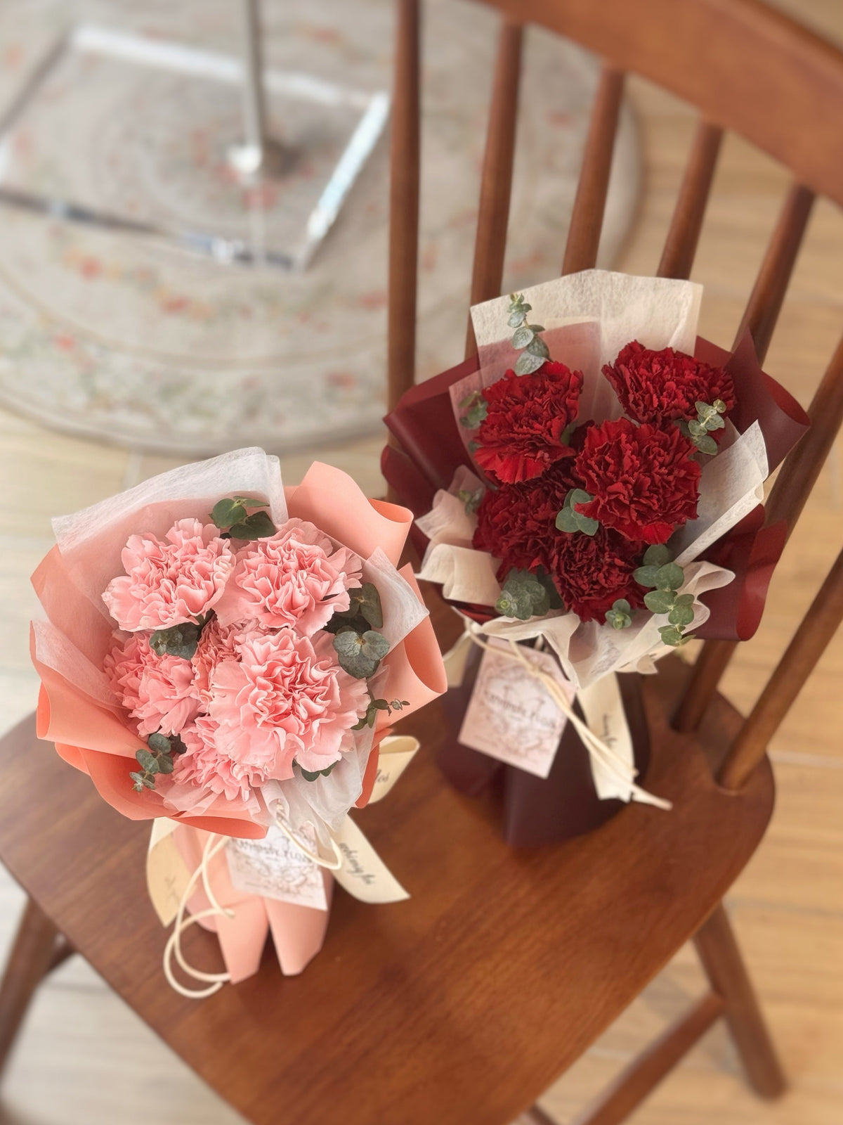 Two bouquets of flowers, one pink and one red, on a wooden chair.
