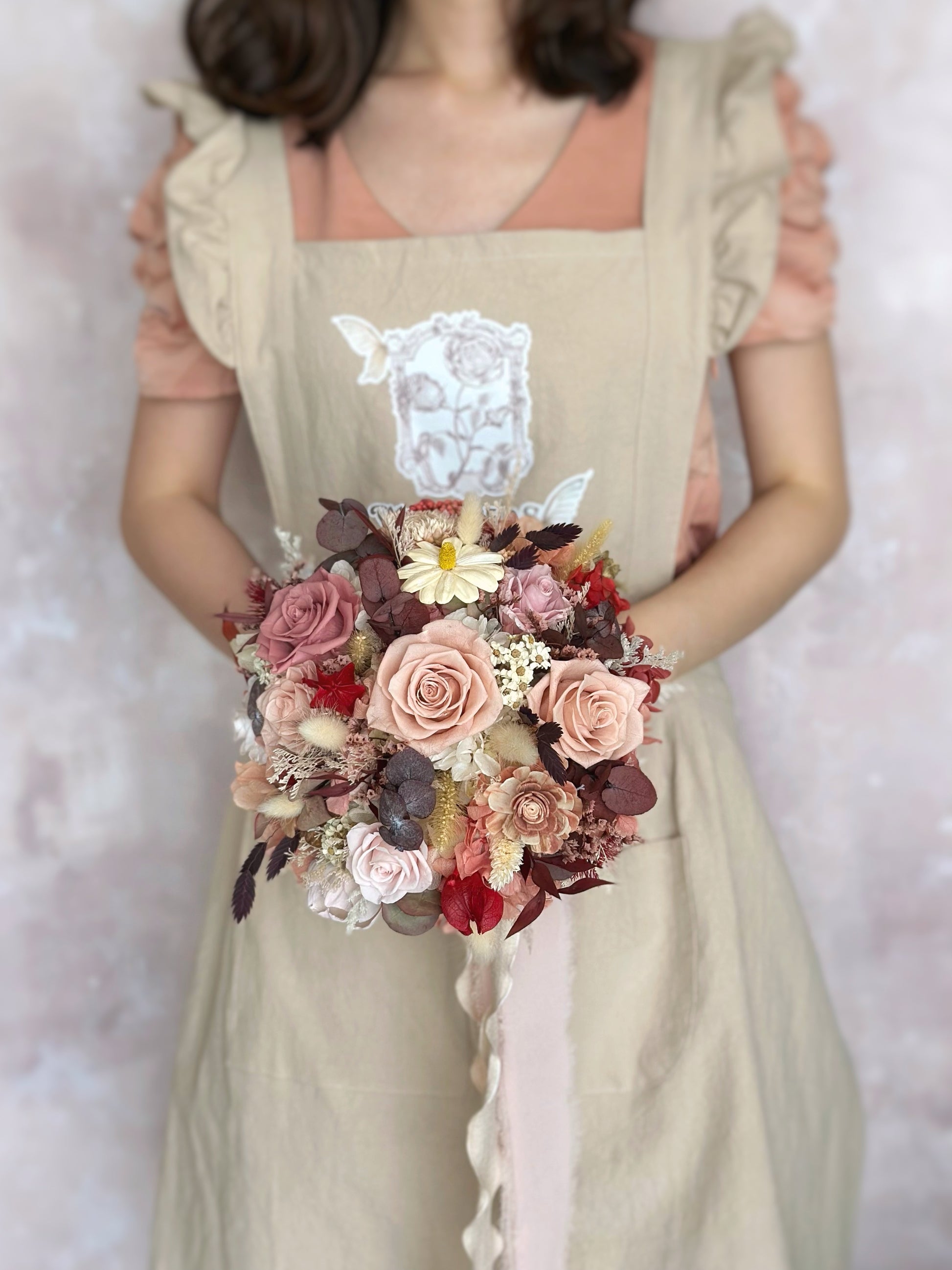 The “Primrose” bouquet held by the bride, its warm hues complementing an autumn-inspired bridal look.
新娘手持“Primrose”捧花，其温暖色调与秋日新娘造型相得益彰。