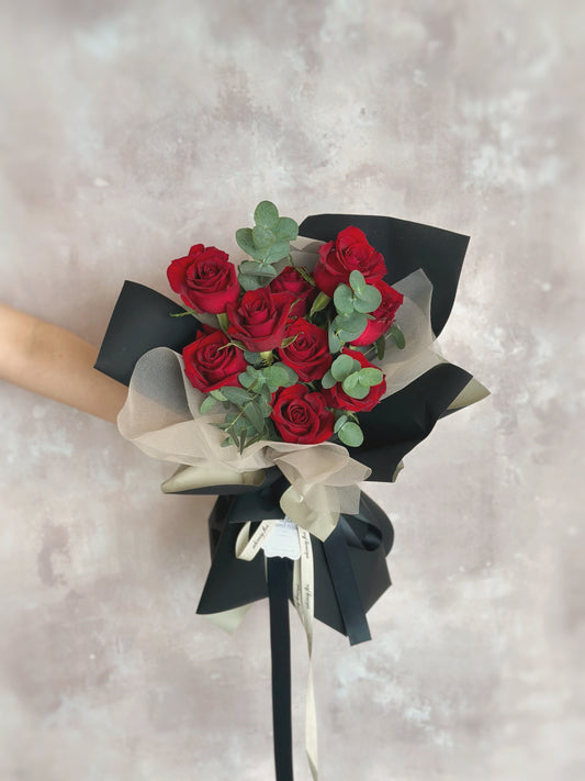 Front view of a modern bouquet with bold red roses and eucalyptus foliage, wrapped in layered black, khaki, and sheer wrapping for contrast and elegance.

正面展示现代感手绑花束，红玫瑰与尤加利叶搭配，采用黑色、卡其与透明包裹，层次分明，气质优雅